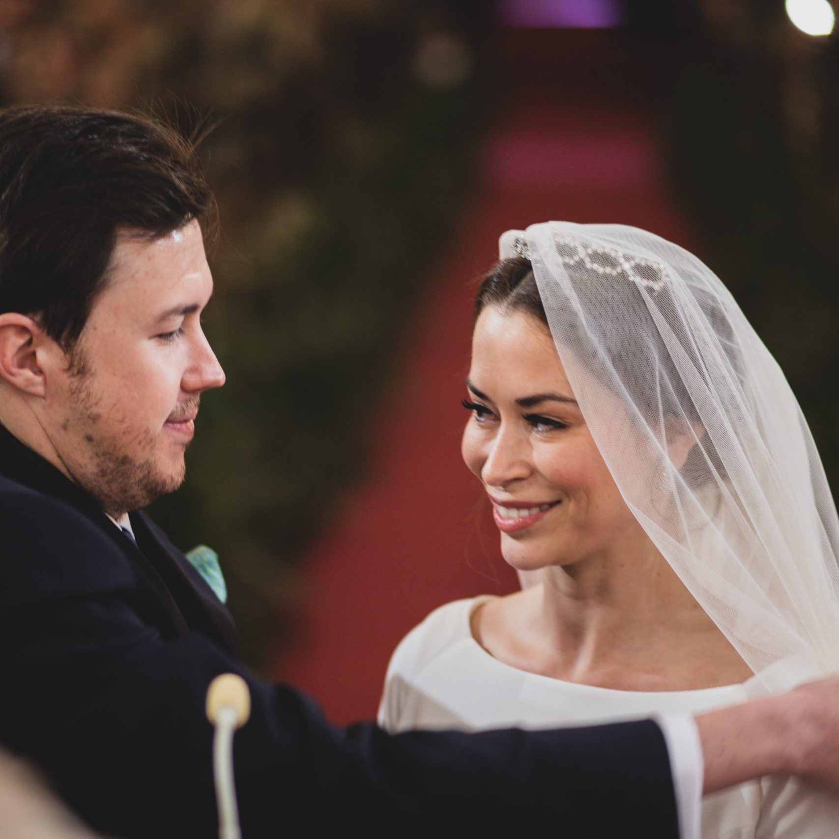 Pareja de novios en la ceremonia, dándose la mano con sonrisas mientras los invitados los observan.