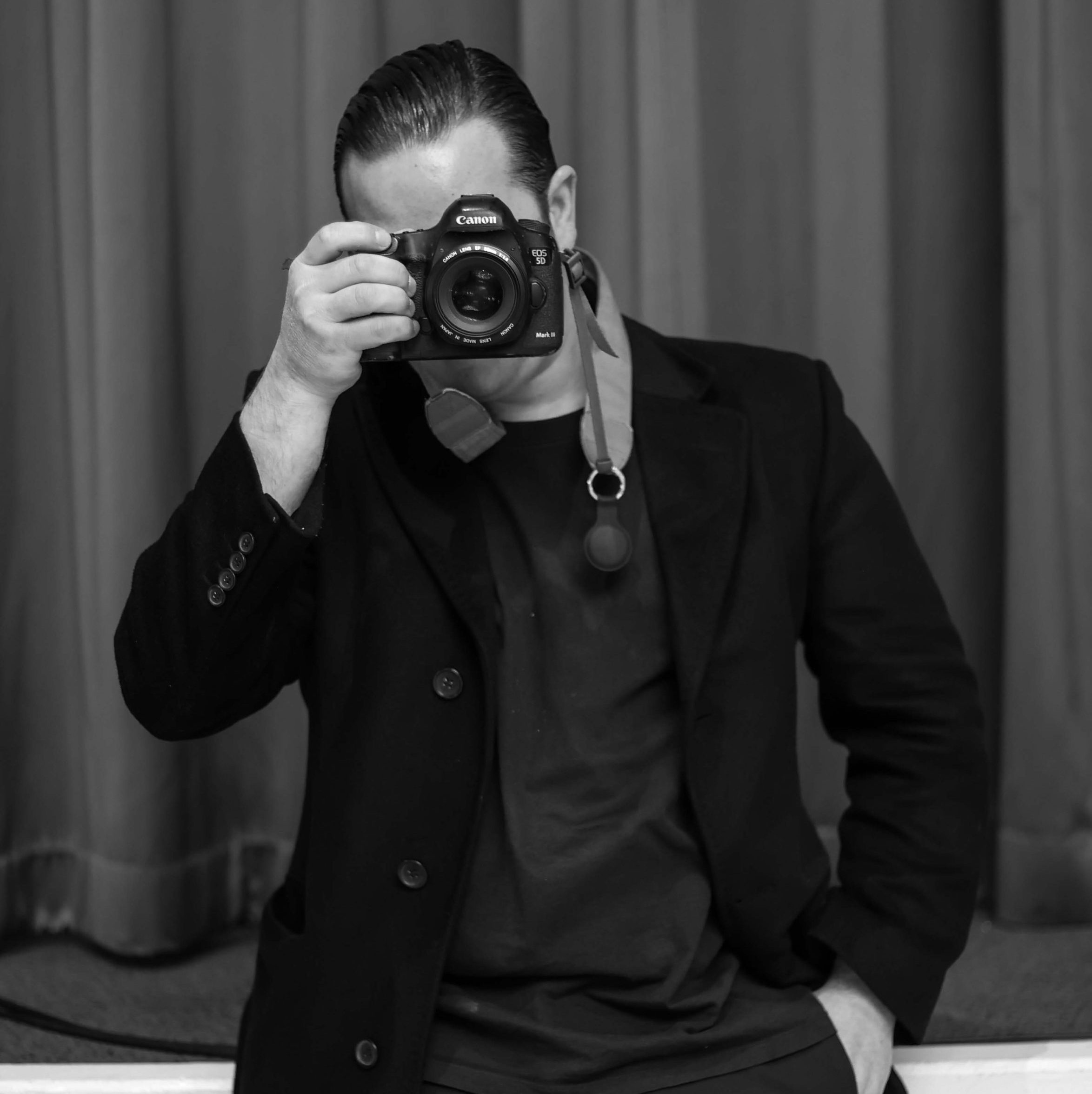 Hombre posando con una cámara en blanco y negro, mirando hacia el lente.