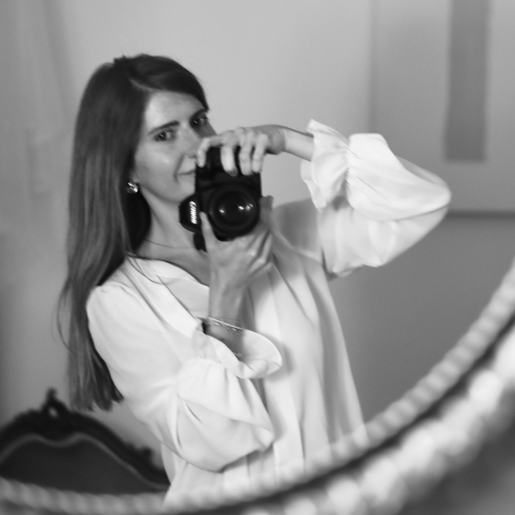 Mujer tomando una foto en blanco y negro frente a un espejo, con una cámara en las manos y una expresión enfocada